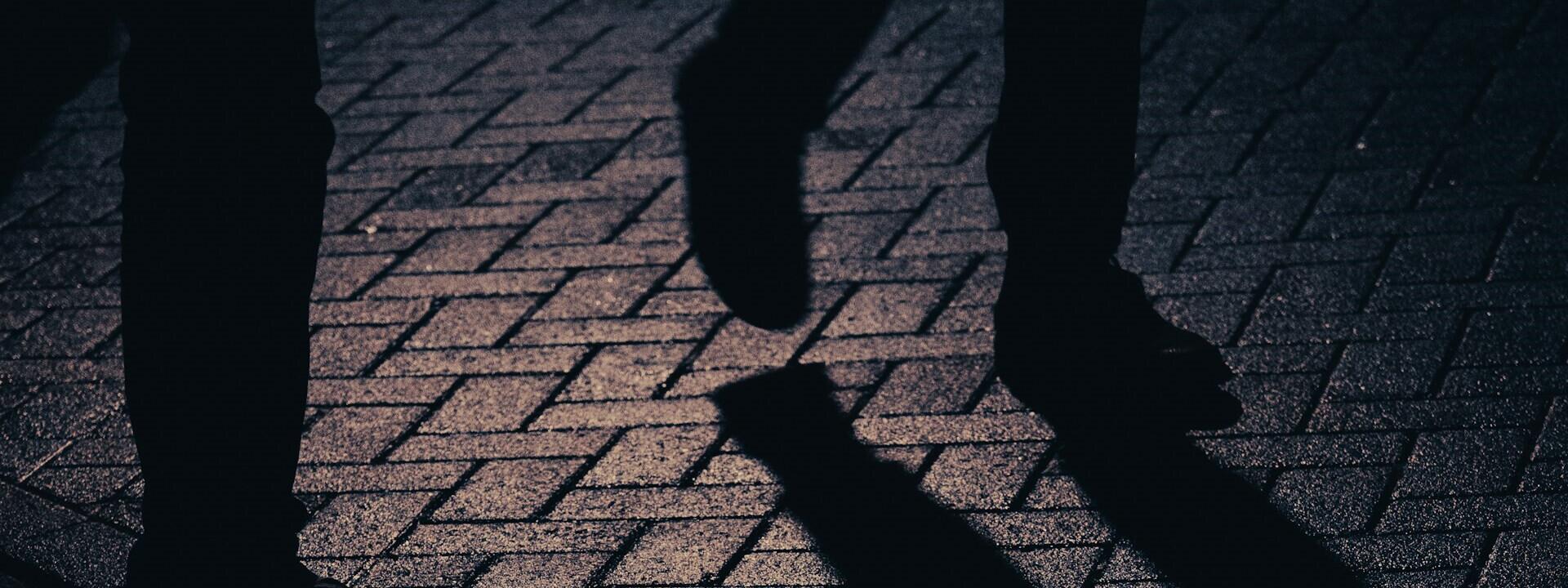 Eine dunkle Straße mit Gestalten, von denen nur die Füße zu sehen sind.