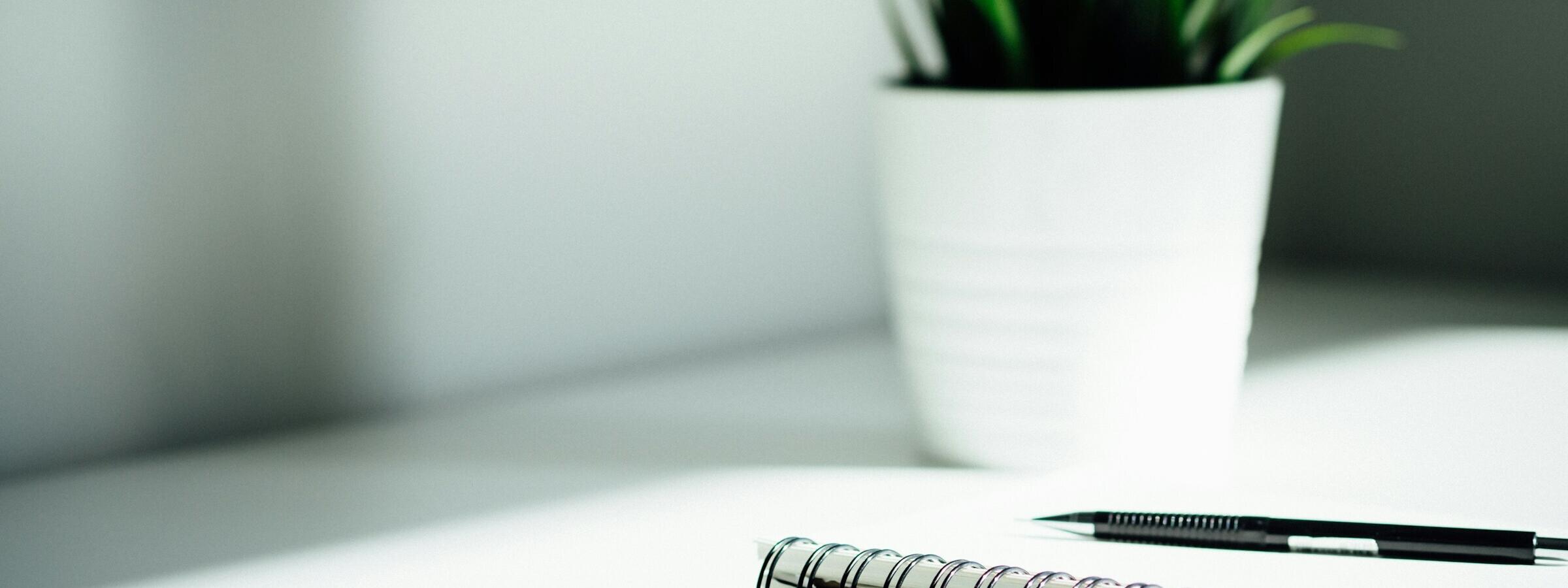Schreibtisch mit Block, Stift und Pflanze