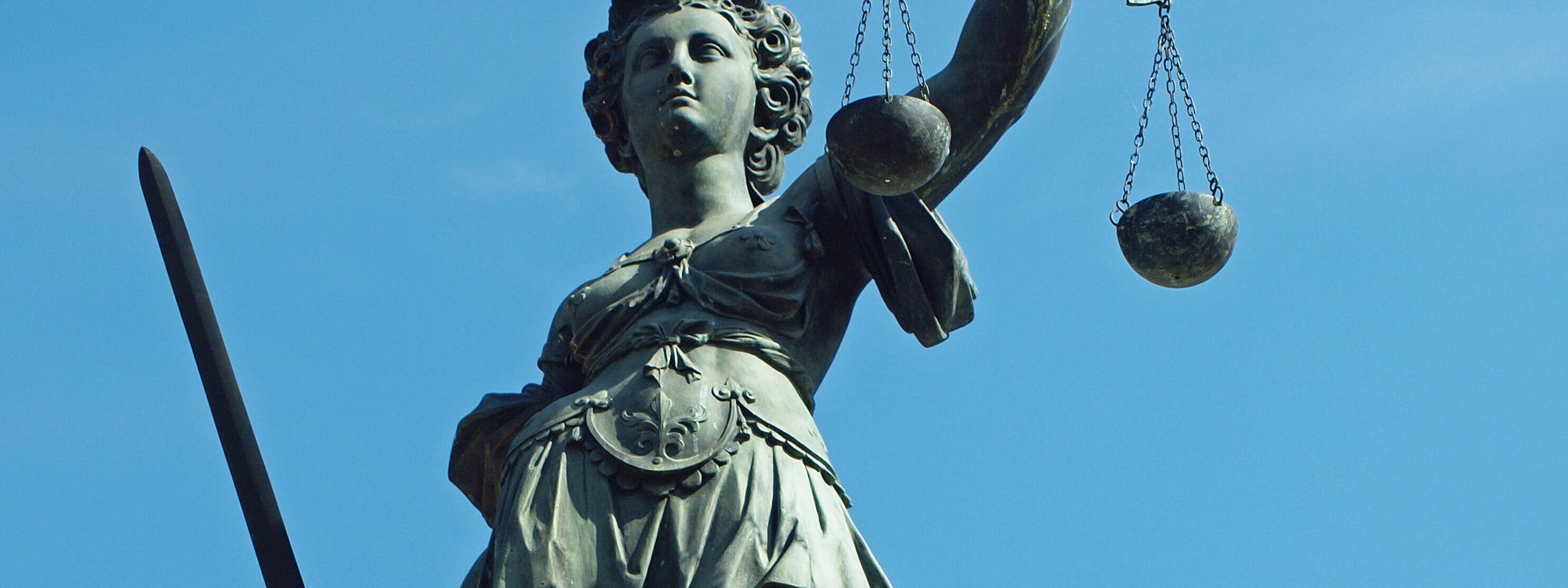 Justitia mit Waage und Schwert vor blauem Himmel
