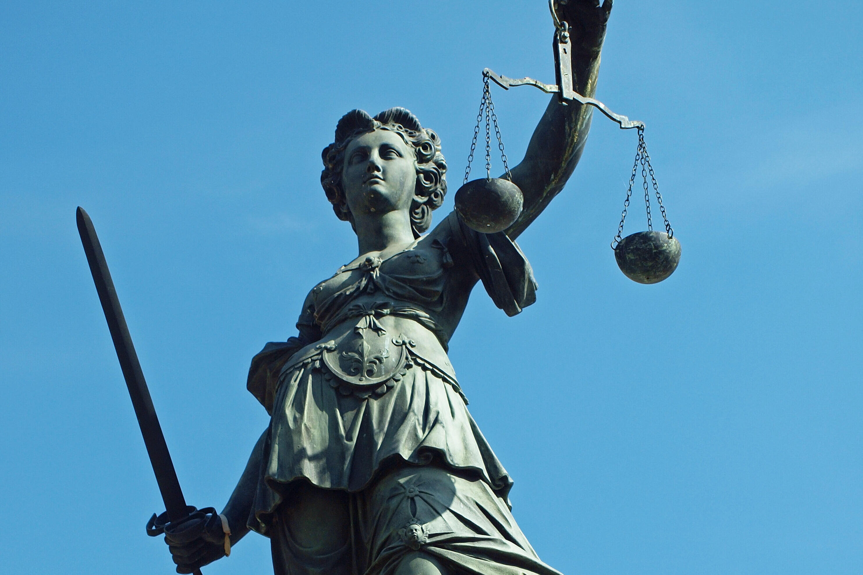 Justitia mit Waage und Schwert vor blauem Himmel