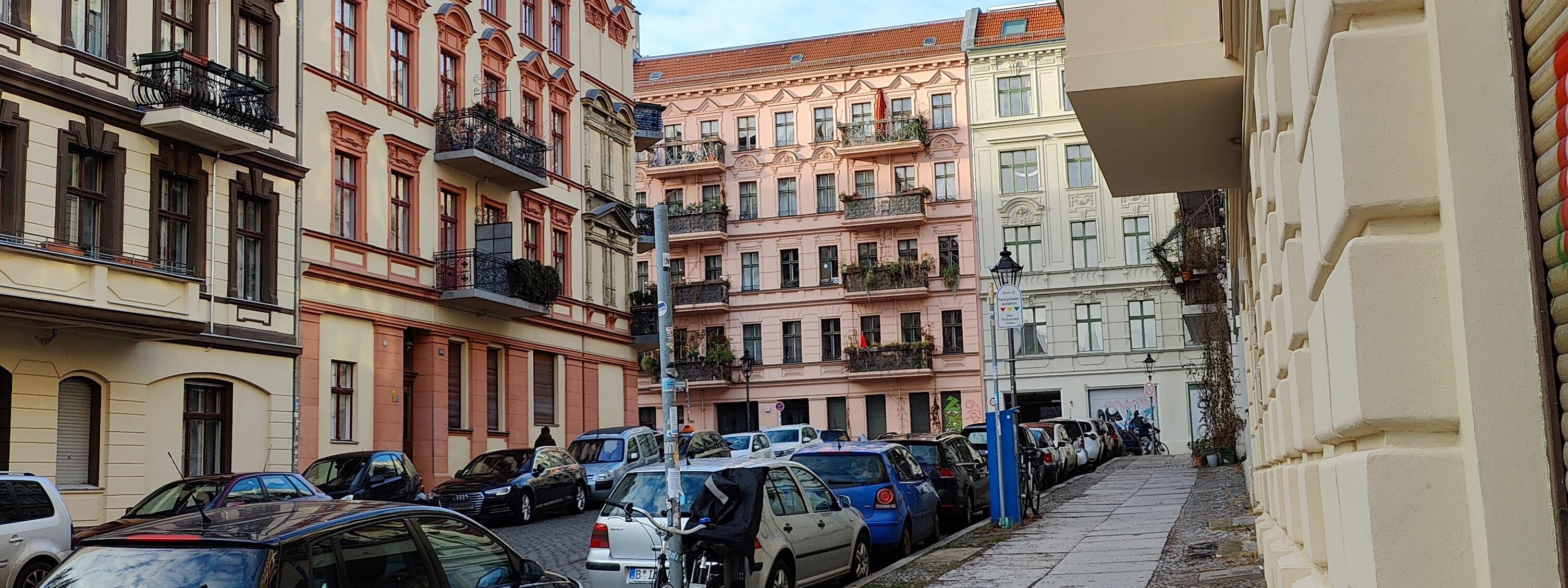 Strassenzug mit Gründerzeithäusern in Berlin. Im Vordergrund stehen Autos.