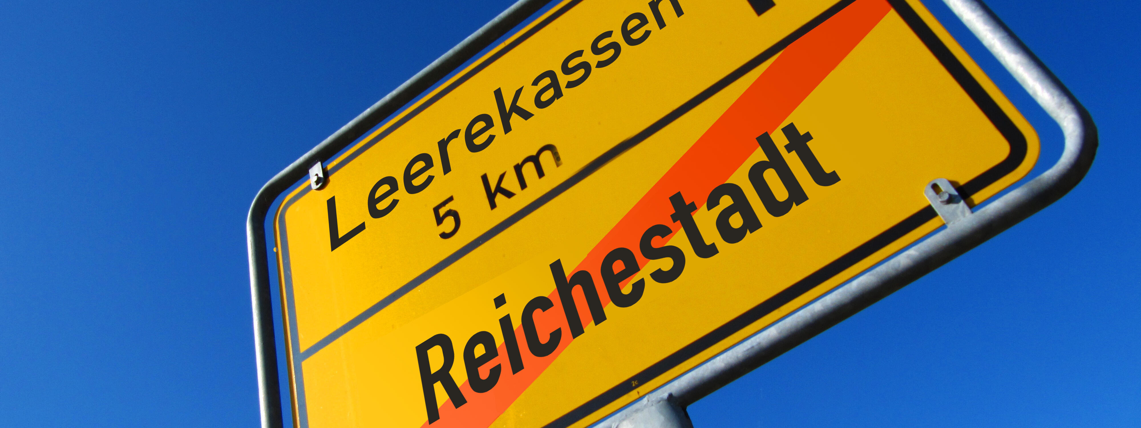 Ein ironisches Ortsschild. Reichestadt ist durchgestrichen. Der Weg führt zu: Leerekassen