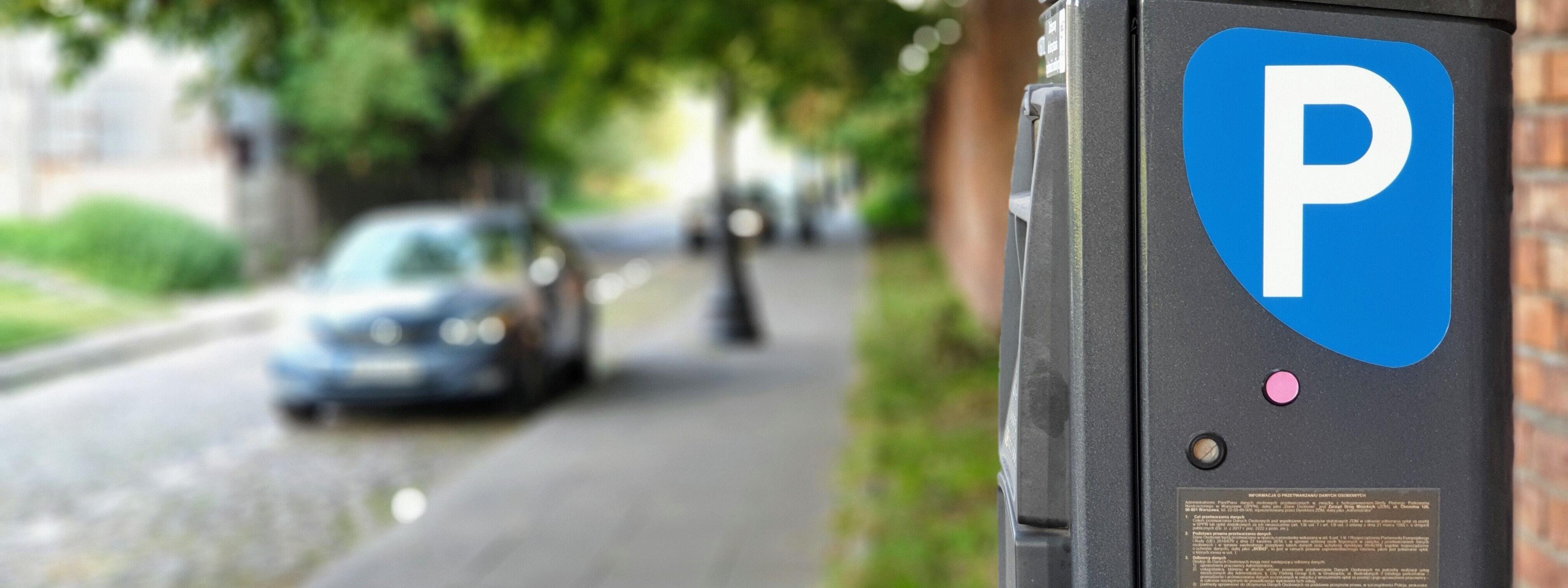 Ein Parkscheinautomat mit einem parkenden Auto im Hintergrund
