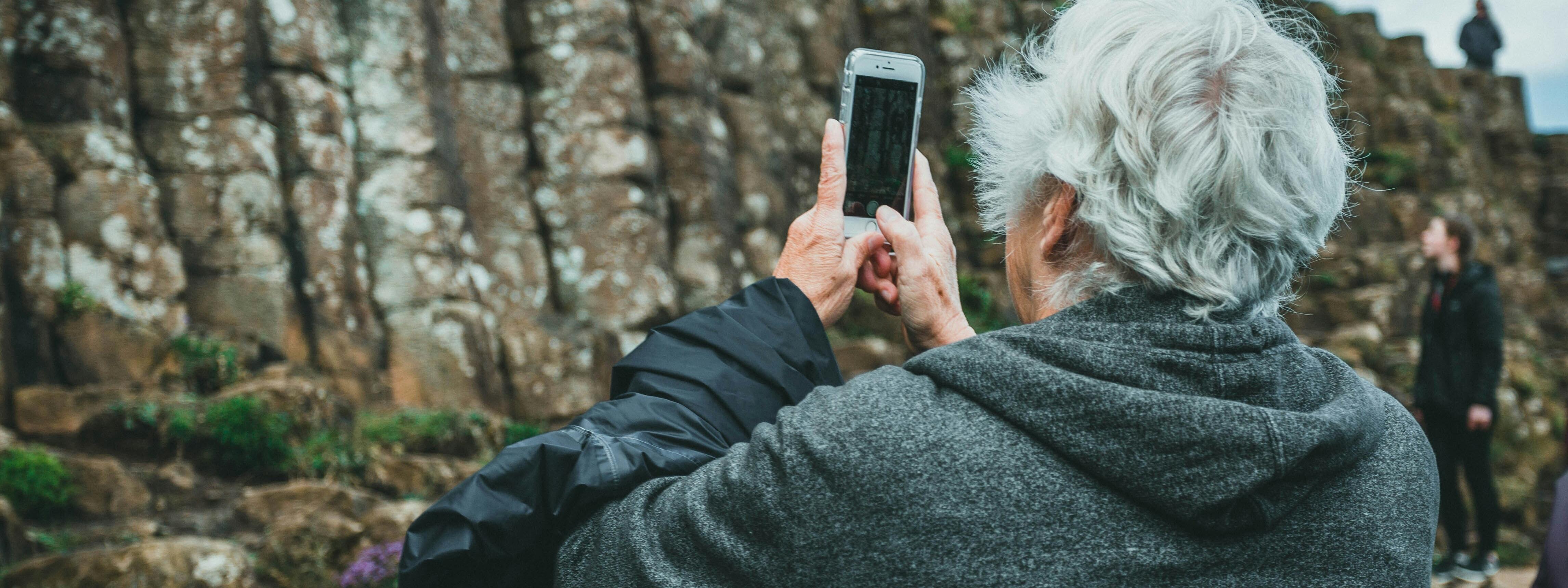 Eine ältere Person fotografiert mit dem Handy eine Wandergruppe an einem Hang.