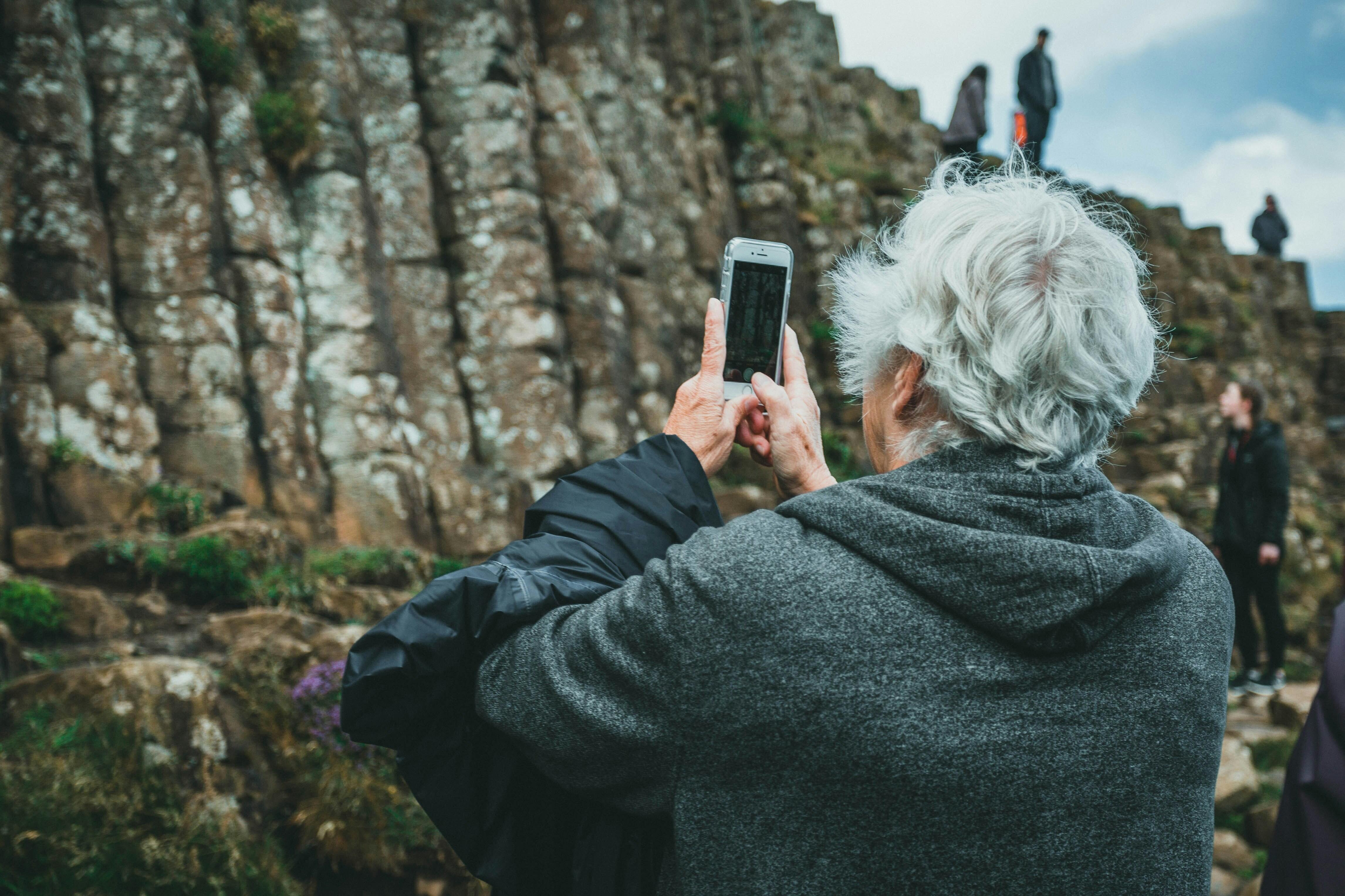 Eine ältere Person fotografiert mit dem Handy eine Wandergruppe an einem Hang.