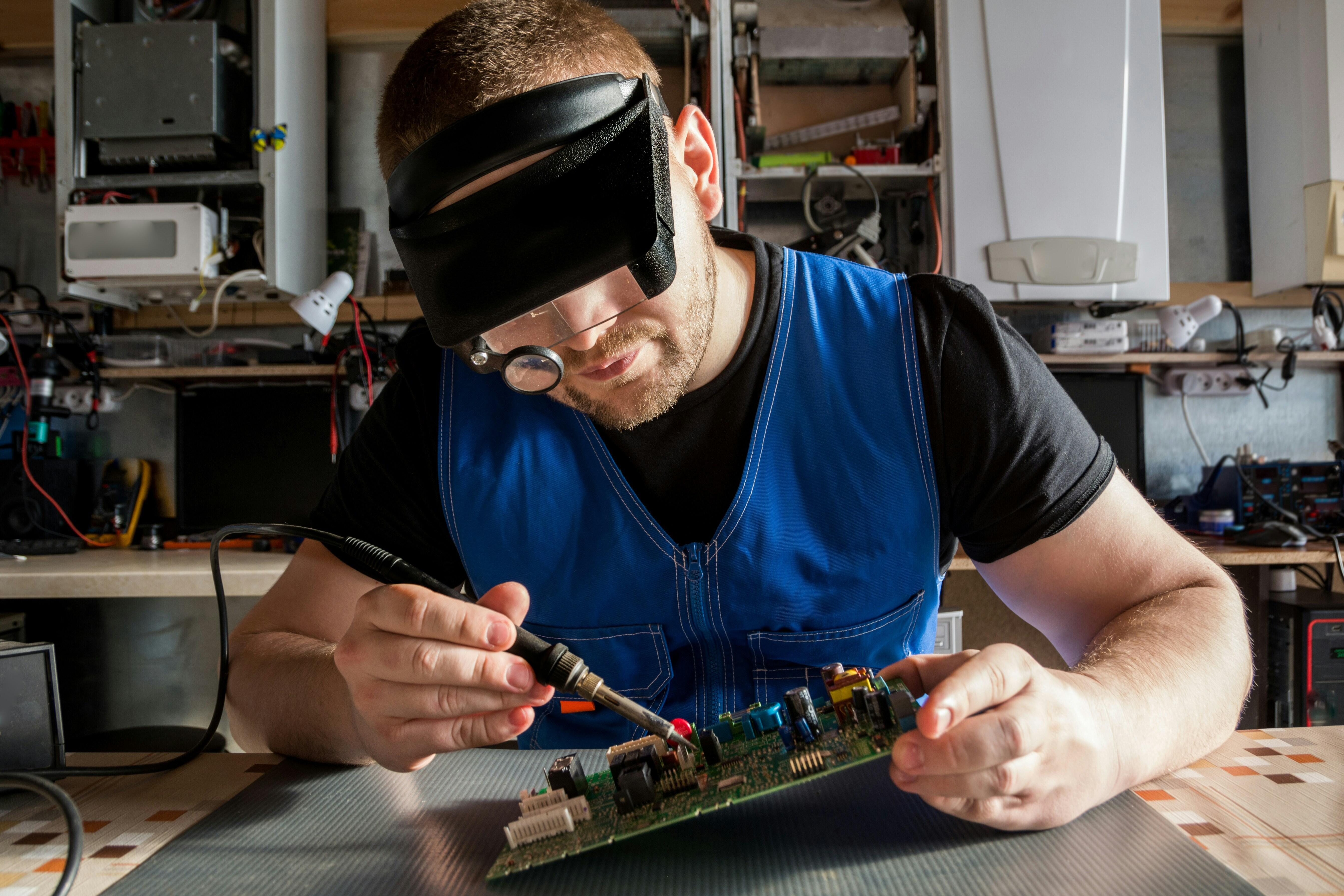 Reparieren statt wegwerfen: Eine Person mit Lupenbrille schraubt an einer Platine