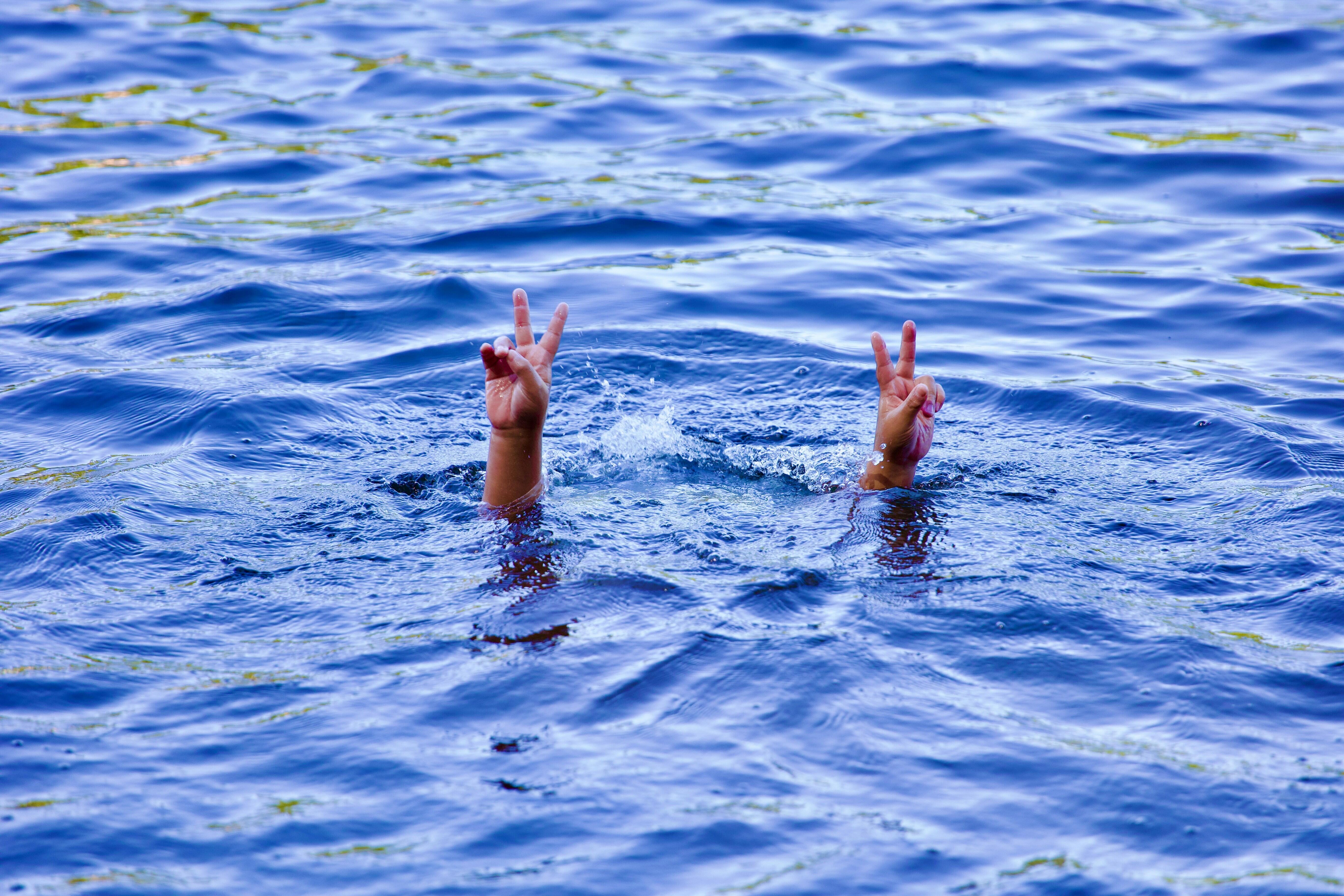 Eine Wasserfläche aus der zwei Hände hervorragen, die ein Victory-Zeichen machen