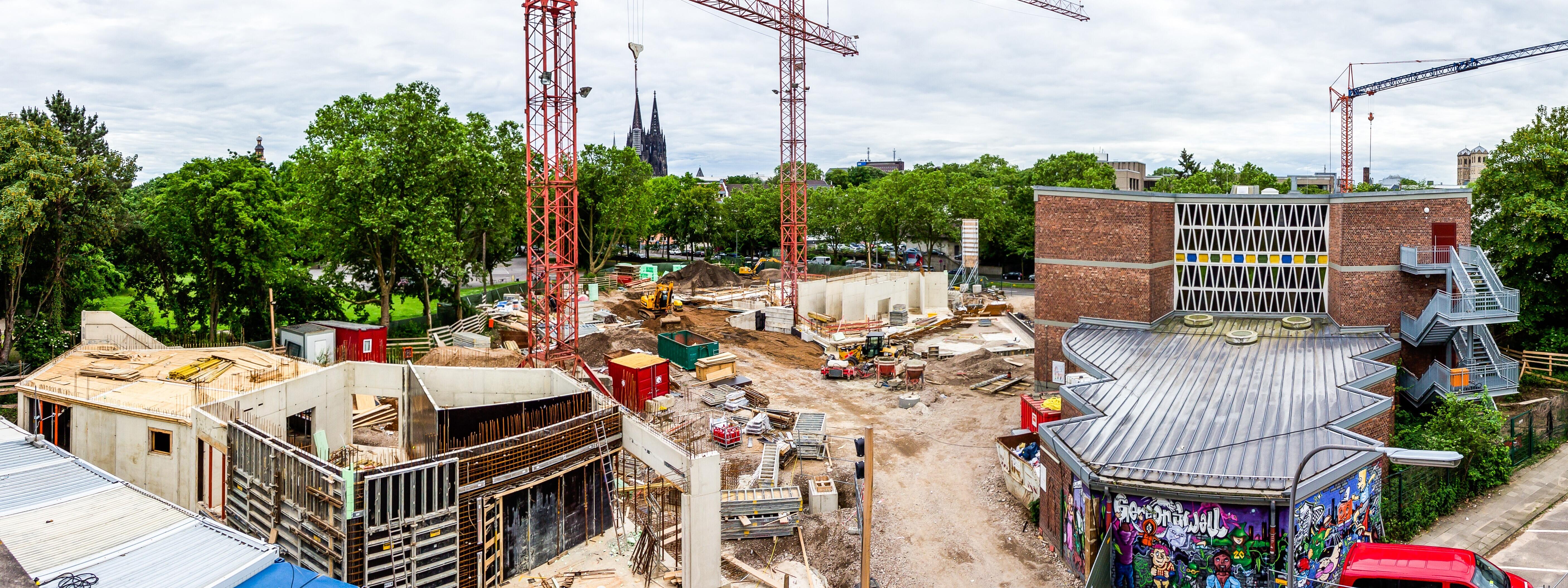 Bildungslandschaft: Die Baustelle einer Schule in Köln mit einem bunten Grafitti im Vordergrund und zwei großen Kränen im Hintergrund