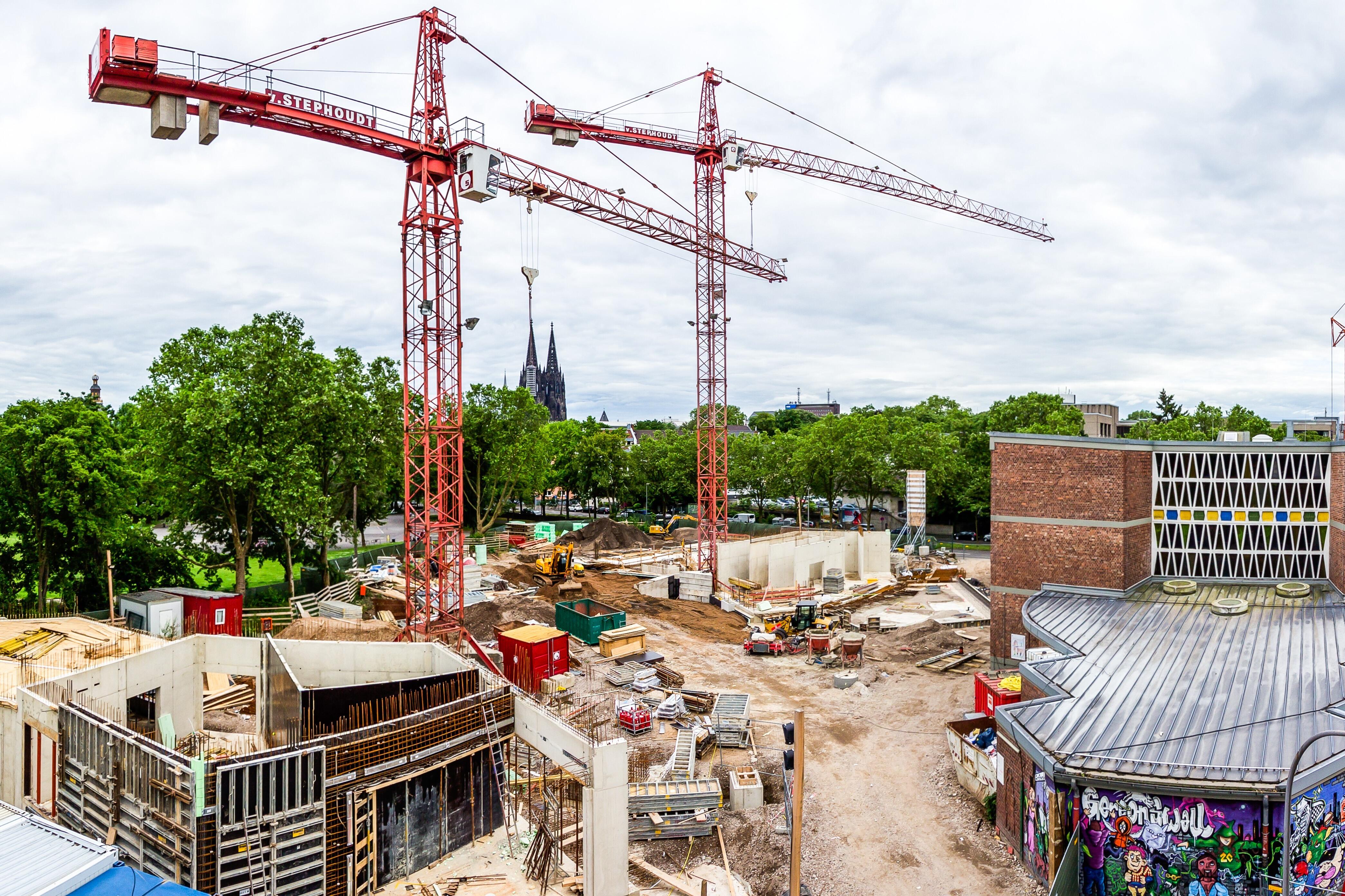 Bildungslandschaft: Die Baustelle einer Schule in Köln mit einem bunten Grafitti im Vordergrund und zwei großen Kränen im Hintergrund