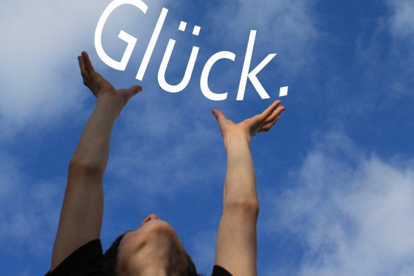 Eine Frau, die das Wort Glück in den blauen Himmel hebt.