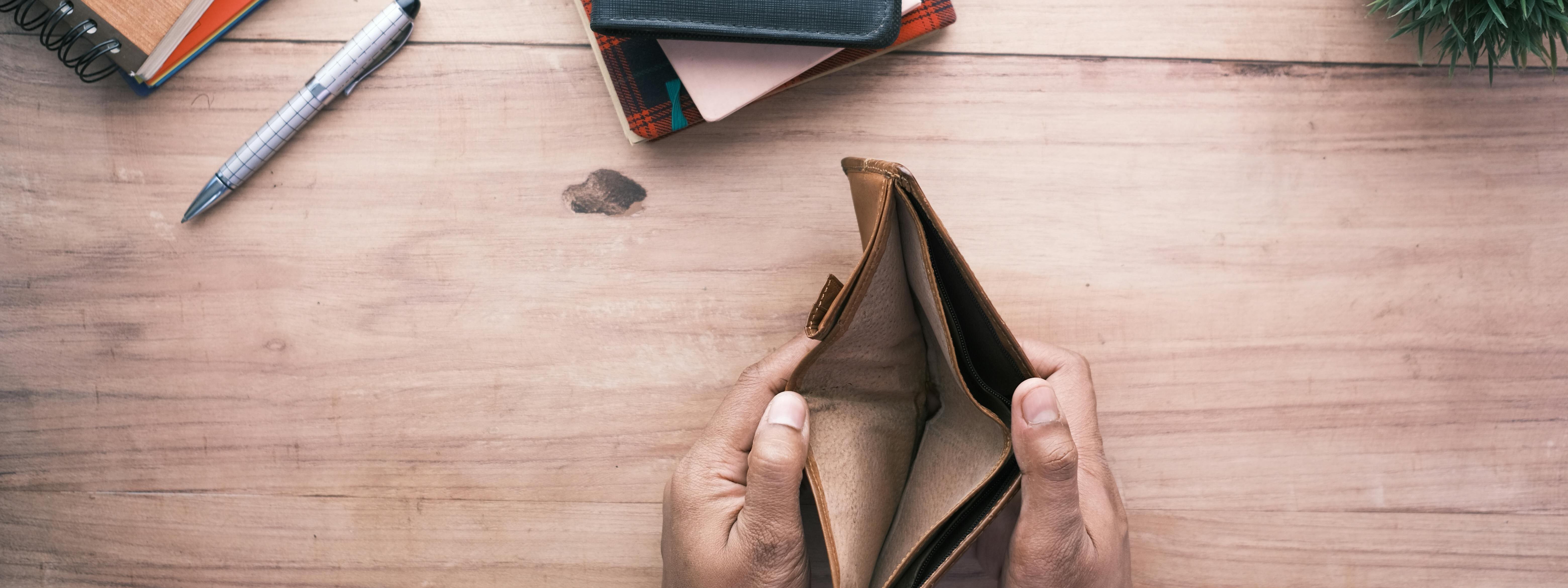 Leeres Portemonnaie auf einem Tisch mit Stift und Notizbüchern.
