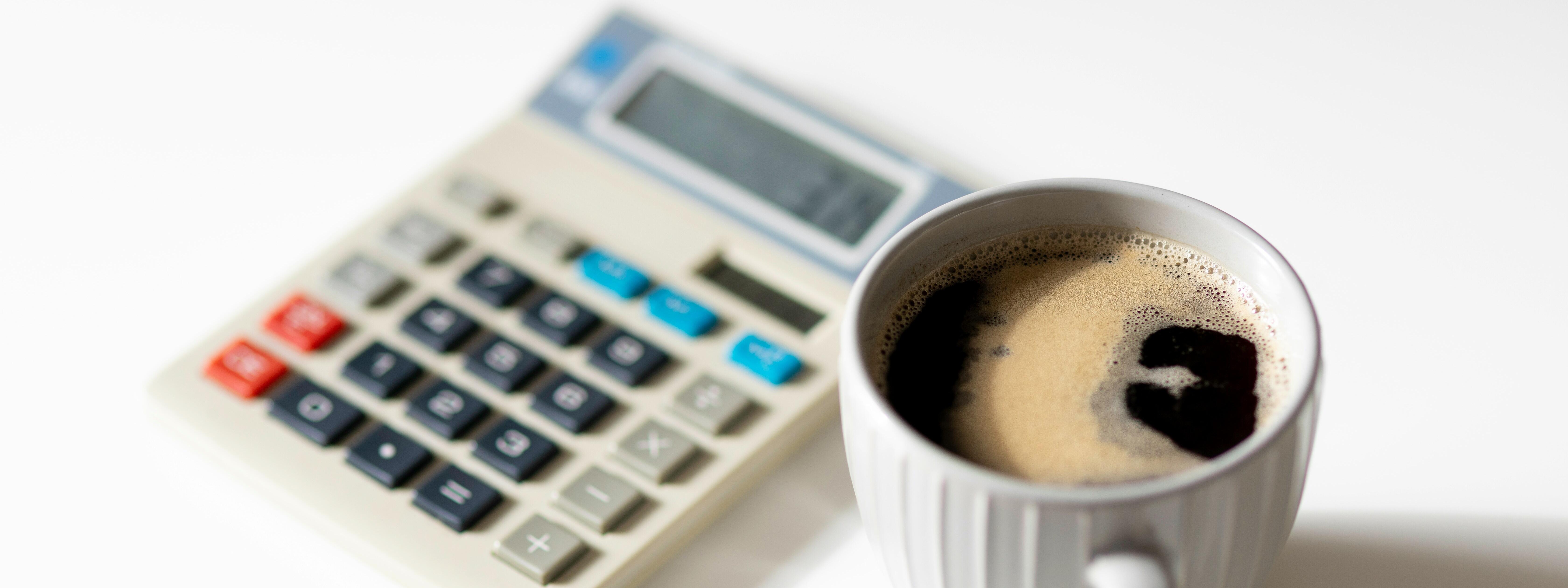 Ein Taschenrechner steht nehmen einer tasse Kaffe. Symbolbild.