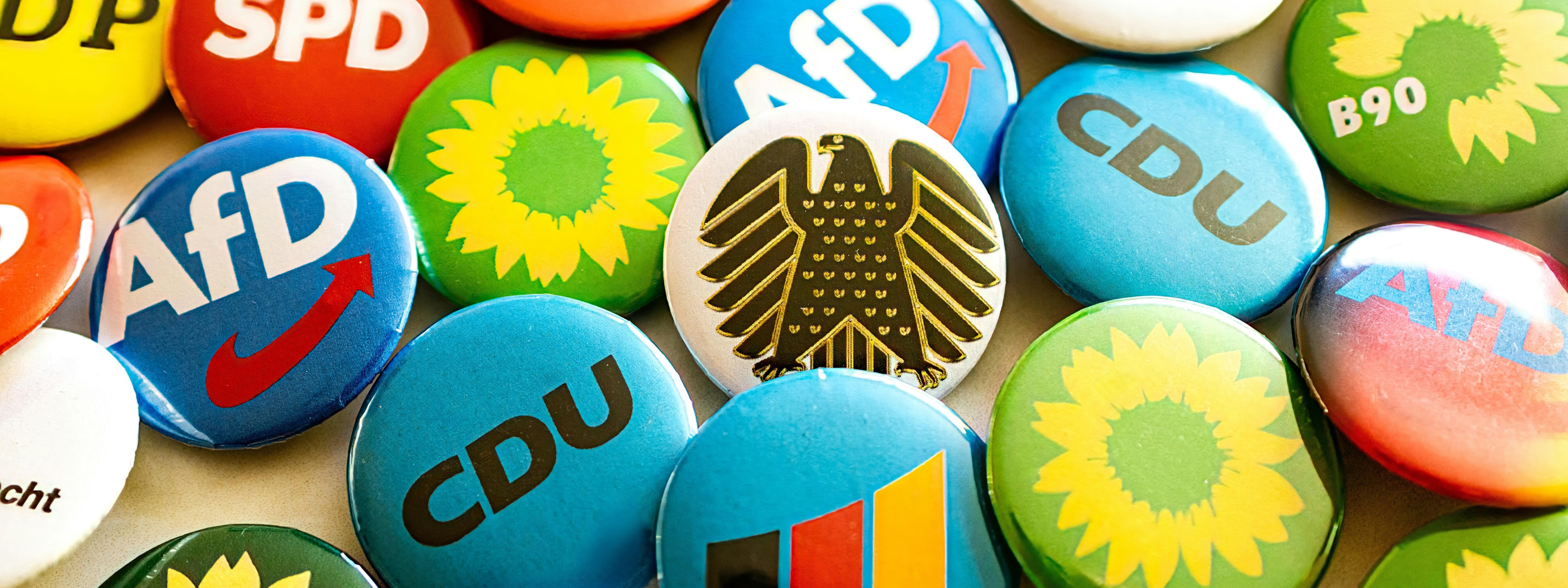 Das Bild zeigt einen Haufen bunter Buttons mit den verschiednenen Parteienlogos.