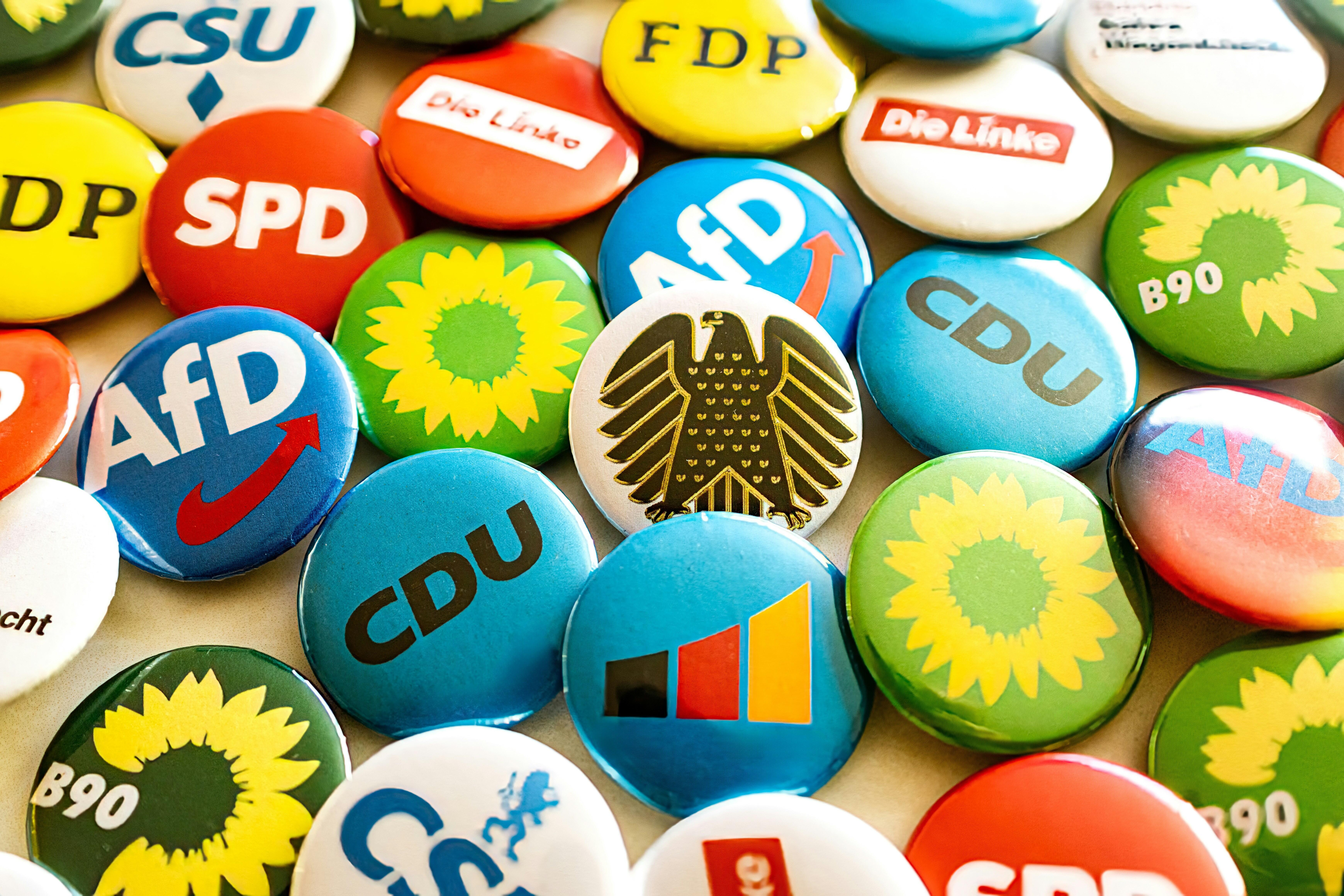 Das Bild zeigt einen Haufen bunter Buttons mit den verschiednenen Parteienlogos.